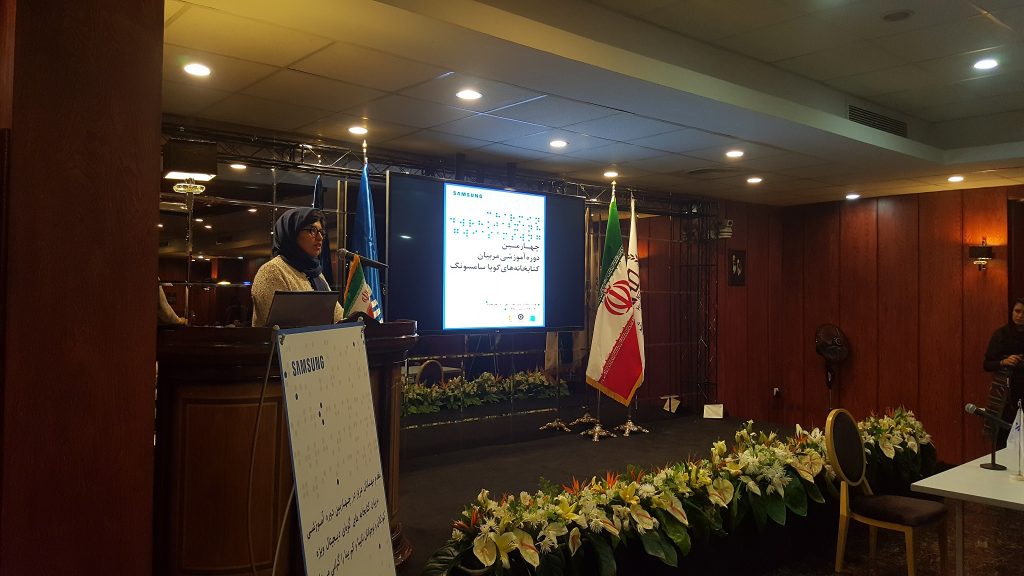 Speaker beside a presentation screen and freestanding Samsung Audio Library sign at the December 2016 ceremony.